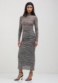 Abito lungo e aderente in una stampa zebra neutra, con maniche lunghe, collo alto e uno spacco laterale, abbinato a tacchi neri con cinghie.