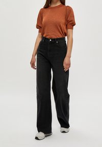 Svart vida jeans med hög midja, tillsammans med en kortärmad, texturerad topp i kopparfärg. Modellen bär grå sneakers.