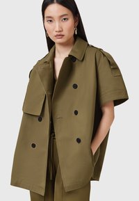 Olive zielona, oversize kurtka z podwójnym zapięciem na guziki, naramiennikami i dwoma przednimi kieszeniami. Teksturowany materiał o gładkim wykończeniu.