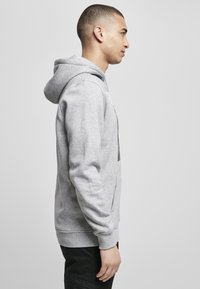 Grå hoodie lavet af blødt bomuldsblend, udstyret med en kengurupose, ribbede manchetter og en justerbar hætte. Enkelt og komfortabelt design.