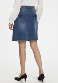 Jeanskjol i en mörkblå tvätt med rak skärning, med bakfickor och gula sömnadsdetaljer. Buren med svarta klackar.