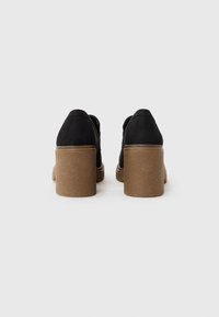 Chaussures à talons en suede noir avec un bout arrondi et une base marron chunky et texturée. Les talons mesurent environ 7,5 cm de haut.