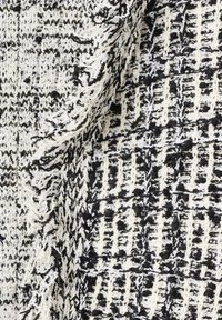 Čierno-biela textúrovaná látka s tkaným vzorom; ošúchané okraje a rôzna hrúbka nití vytvárajú dotykový povrch.