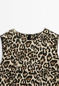 Yksivärinen leopardi-tulostoppi, jossa on pyöreä pääntie, hihaton muotoilu ja kevyt kangas, jossa on tummanruskeita ja mustia kuvioita.