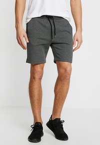 Pantaloni sportivi grigi con vita regolabile tramite coulisse, tasche laterali e un morbido tessuto misto. Indossati con scarpe sportive nere.