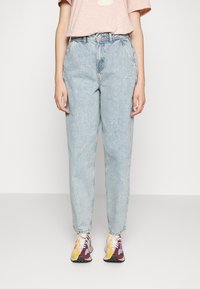 Jean de cintura alta, azul claro, com um corte relaxado, ligeiramente desgastado e uma textura suave, combinado com ténis multicoloridos e uma t-shirt rosa.