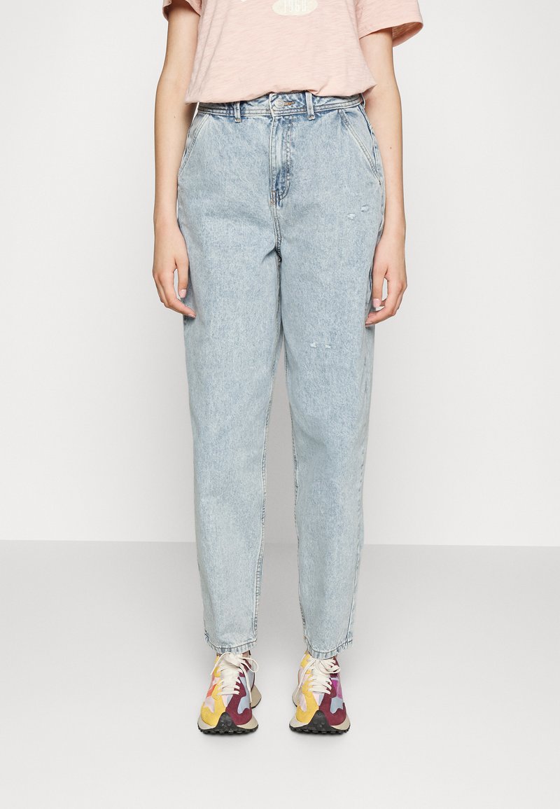 Jean de cintura alta, azul claro, com um corte relaxado, ligeiramente desgastado e uma textura suave, combinado com ténis multicoloridos e uma t-shirt rosa.