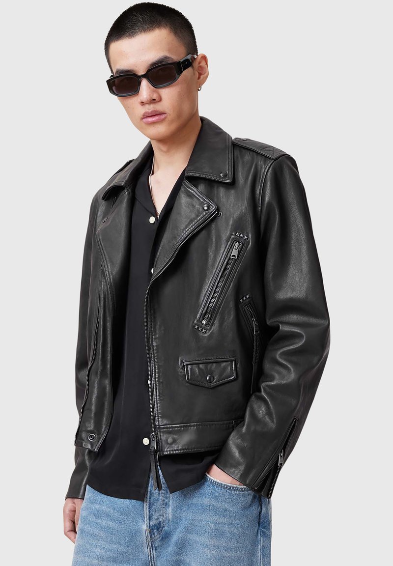 Schwarze Leder-Motorradjacke mit Reißverschlüssen, Druckknöpfen und Seitentaschen. Sie verfügt über einen spitzen Kragen und ein tailliertes Design.