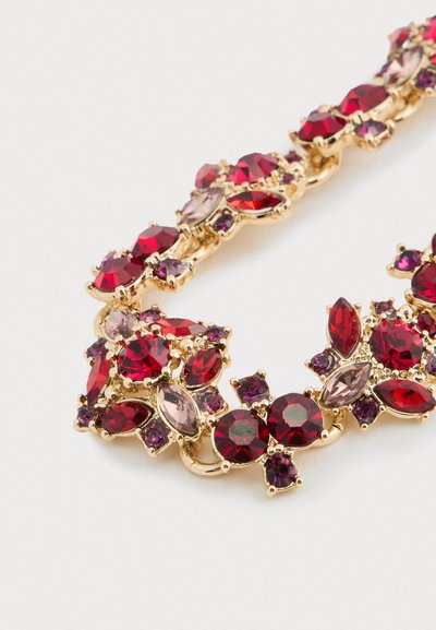 Zlatá náhrdelník s klastry červených, růžových a fialových fasetovaných drahokamů různých tvarů na bílem pozadí.