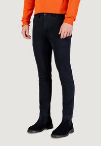 Pantalon noir ajusté en coton à la texture lisse, associé à des bottines noires à hauteur de cheville et un pull orange.