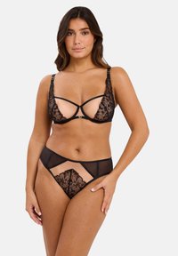 Soutien-gorge en dentelle noire et string assorti. Le soutien-gorge a des panneaux transparents, une broderie florale et des bretelles ajustables. Le string présente des découpes géométriques et des accents en dentelle.