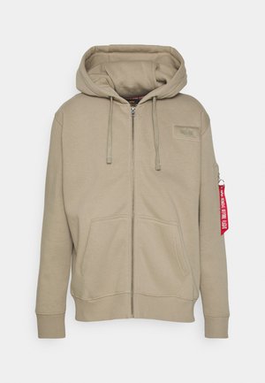 Khaki zip-up hoodie med foret hætte, frontlommer, ribbede manchetter og et mærke på brystet. Har et rødt mærke på venstre ærme.
