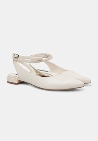 Bijele kožne slingback cipele s šiljastim nosom, malom blok petom i križnim remenom oko gležnja. Glatka tekstura i minimalna detalj.