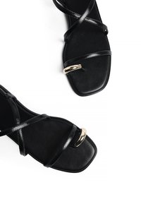 Mustad mustad hõbedega sandaalid, millel on läikiv rihmade disain, ruudukujuline varvas ja silmatorkav kuldse tooni detail esiküljel.