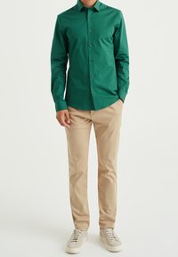 Grön skjorta med knappar, slätt tyg, långa ärmar. Beige chinos, bomullsmaterial, slim fit. Ljusgrå sneakers med en texturerad yta.