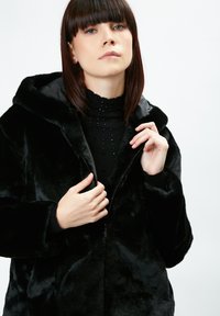 Sort faux fur-jakke med hætte, med lynlåslukning og struktureret overflade. Lange ærmer og en afslappet pasform.