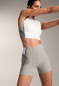 Sport felső és magas derekú rövidnadrág bézs és fehér színben, türkiz részletekkel. Az anyag sima, testhezálló kialakítással és varrás nélküli szélekkel rendelkezik.