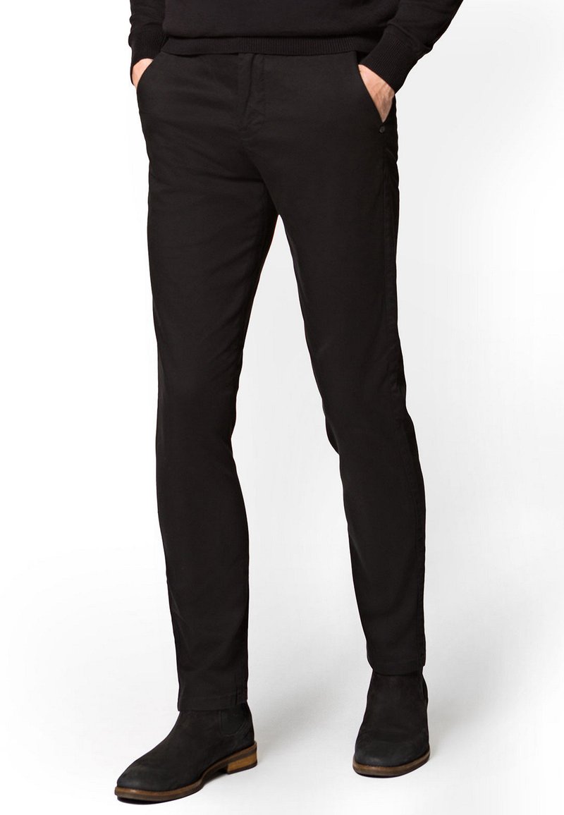 Czarne, dopasowane spodnie wykonane z bawełny. Posiadają dwie boczne kieszenie i gładką teksturę, w zestawie z czarnymi botkami za kostkę.