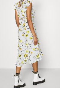 Florales Midikleid mit hellblauem Hintergrund, grünem und gelbem Blumenmuster, Rüschenärmel und einem ausgestellten Saum, kombiniert mit weißen Combat-Stiefeln.