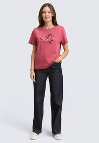 Short-sleeve, rose-colored t-shirt with a black floral print design, paired with dark blue jeans and white sneakers. Soft cotton material.
