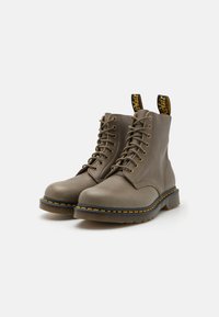 Botas de tobillo con cordones en cuero taupe, con costuras amarillas a lo largo de la suela, punta redonda y tiradores negros con el logo de la marca.