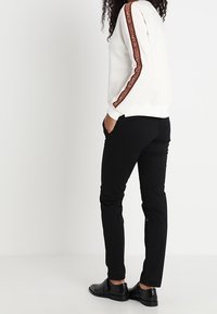 Felpa bianca con striscia accentata marrone lungo le maniche, abbinata a pantaloni neri e scarpe nere lucide. Fit casual con polsini a coste.