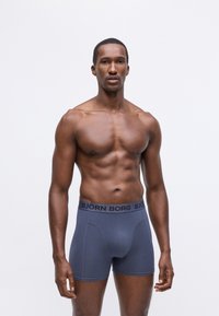 Muška bokserice u plavoj boji s tamnim elastičnim pojasom označenim "BJÖRN BORG." Tkanina izgleda glatko s prilagođenim dizajnom.