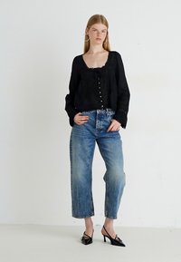 Blusa nera a maniche lunghe con chiusura a bottoni e dettagli in pizzo, abbinata a jeans a gamba dritta in denim chiaro a vita alta e tacchi neri.