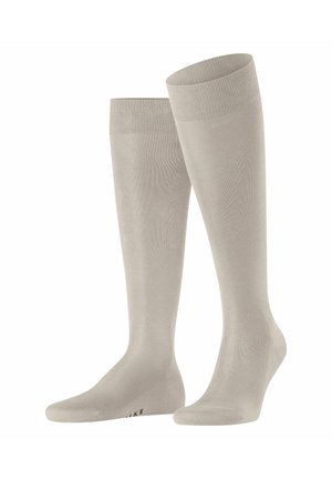 Paar hellbeige kniehohe Kompressionsstrümpfe mit glatter Textur und gerippten Bündchen, aufrecht auf weißem Hintergrund platziert.