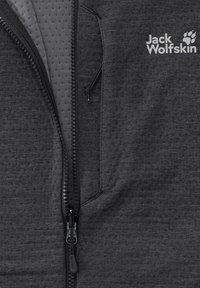 Grijze fleecejas met een gestructureerd oppervlak, ritssluiting aan de voorkant en contrasterende voering aan de binnenkant. Heeft een logo aan de bovenkant aan de linkerkant.