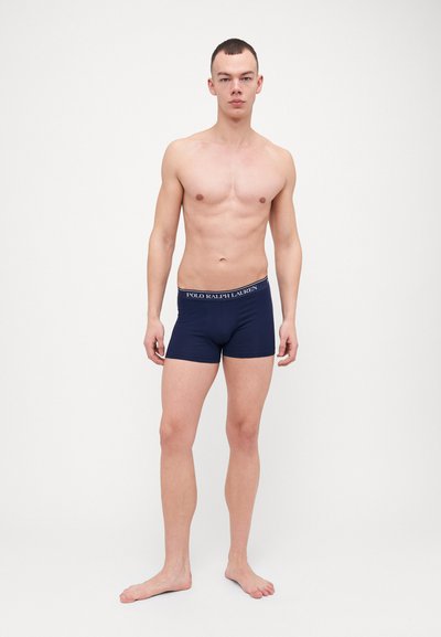 Boxeri de culoare albastru marin, realizați dintr-un material elastic cu un brâu elastic, având un logo alb "Polo Ralph Lauren". Modelul stă desculț.