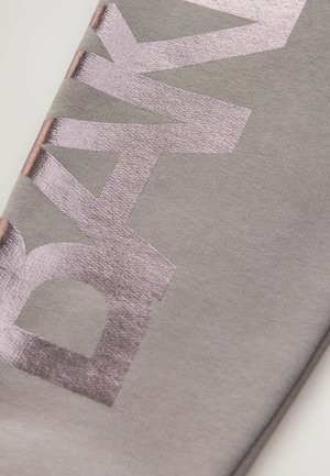 Gråt stof med skinnende rosaguldtekst, der staver "BAK" på tværs af et diagonalt mønster. Blød tekstur med en glat overflade.