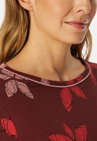Bordeaux top met bloemenprint in rood en roze. Kenmerken een ronde halslijn met een contrasterende lichtroze rand. Zacht, gestructureerd stof.