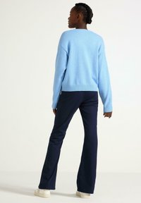 Lyseblå strikket sweater med en afslappet pasform, parret med mørkeblå flagrende bukser. Sweateren har ribkantede manchetter og kant.