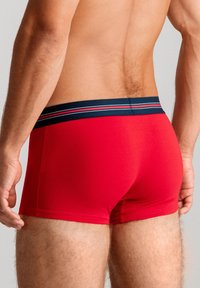Röda boxershorts med en marinblå midja som har tre ränder. Materialet verkar glatt med en åtsittande passform och har en minimalistisk design.