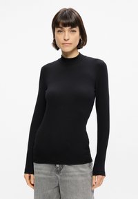 Melna gara piedurkne turtlenecka blūze, izgatavota no gludas, elastīgas auduma. Pieguļošs dizains ar minimālu šuvju skaitu, apvienota ar gaiši pelēkiem platām kājām džinsiem.