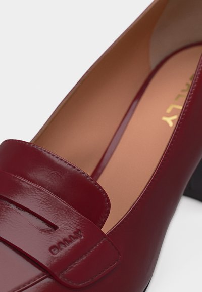 Gros plan sur un mocassin pour femme en cuir rouge foncé poli, avec un petit talon et une couture de marque sur la lanière.