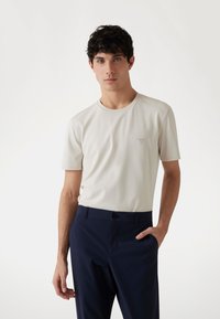 Hellgraues Kurzarm-T-Shirt mit rundem Hals und einem kleinen dreieckigen Logo auf der Brust, kombiniert mit dunkelblauen Hosen.
