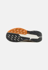 Skoens sål har en struktureret sort gummibase med en orange midtersektion, som viser trekantede dækmønstre og et logodetalje.