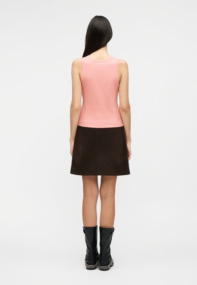 Γυναίκα γυρισμένη με την πλάτη φοράει ένα ροζ αμάνικο τοπ, καφέ σκουρόχρωμη φούστα μέχρι το γόνατο και μαύρες μπότες μέχρι τη μέση της γάμπας με αλυσίδα διακόσμηση.