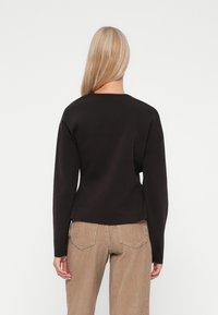 Donkerbruin trui met lange mouwen, geribbelde halslijn en een ontspannen pasvorm, gedragen met beige corduroy broek met achterzakken.