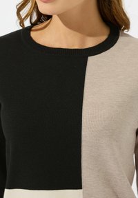 Maglione lavorato a maglia con un design a colori bloccati in sezioni nere, marrone chiaro e crema. Collo rotondo con finiture a coste, texture morbida.
