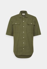 Kurzarmhemd aus dunkelgrünem Stoff mit Knopfleiste, zwei Brusttaschen und abgerundetem Saum. Sanfte Textur, lässiges Design.