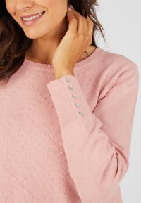 Maglione rosa chiaro con un motivo testurizzato e scollatura rotonda. Presenta dettagli con bottoni sulle maniche. Materiale in maglia morbida, maniche lunghe.