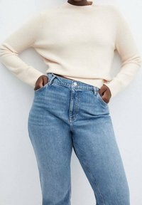 Light beige knit sweater with a crew neck, paired with high-waisted blue denim jeans. Jeans feature front pockets and a button closure.