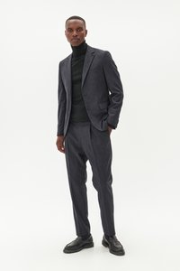 Traje navy de tela texturizada, con chaqueta ajustada y pantalones slim fit, complementado con un suéter de cuello alto negro y zapatos negros.