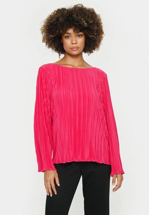 Langsleeve blouse in felroze, met een geplooide textuur, losse pasvorm en ronde halslijn. Gecombineerd met zwarte broeken.