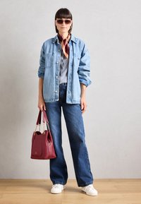 Veste en denim, t-shirt gris, jeans à jambes larges, baskets blanches, sac bordeaux avec des accents en chaîne et lunettes de soleil. Textures lisses et style décontracté.