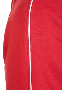 Vêtement rouge en tissu tricoté texturé, avec une bande blanche contrastante sur un côté. Design simple sans décorations supplémentaires.