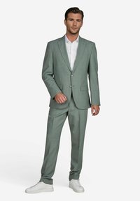 Lichtgroen pak van gestructureerde stof, bestaande uit een single-breasted blazer, bijpassende broek en witte sneakers.